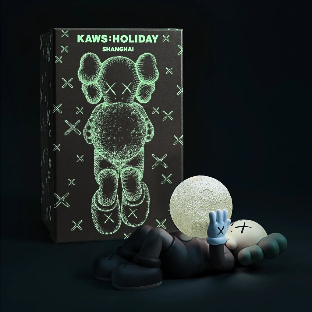 KAWS SHANGHAI figure in Brown lying next to its packaging box, which features a glow-in-the-dark design of the Companion holding a moon.