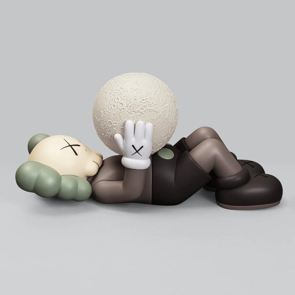 KAWS SHANGHAI figure in Brown lying down, holding a textured moon with both hands, against a light gray background.