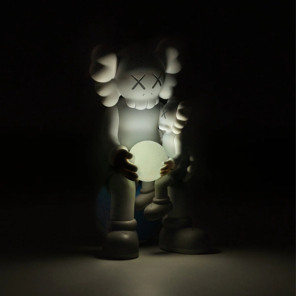 kaws:HOLIDAY THAILAND Grey figure in darkness with glowing moon effect, highlighting emotional embrace between Companions.