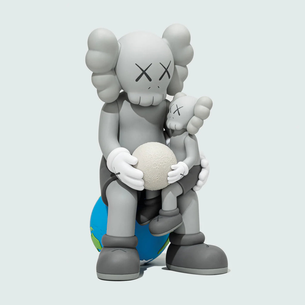 Side angle of KAWS:HOLIDAY THAILAND Grey collectible showing adult Companion embracing child, both holding a textured moon.