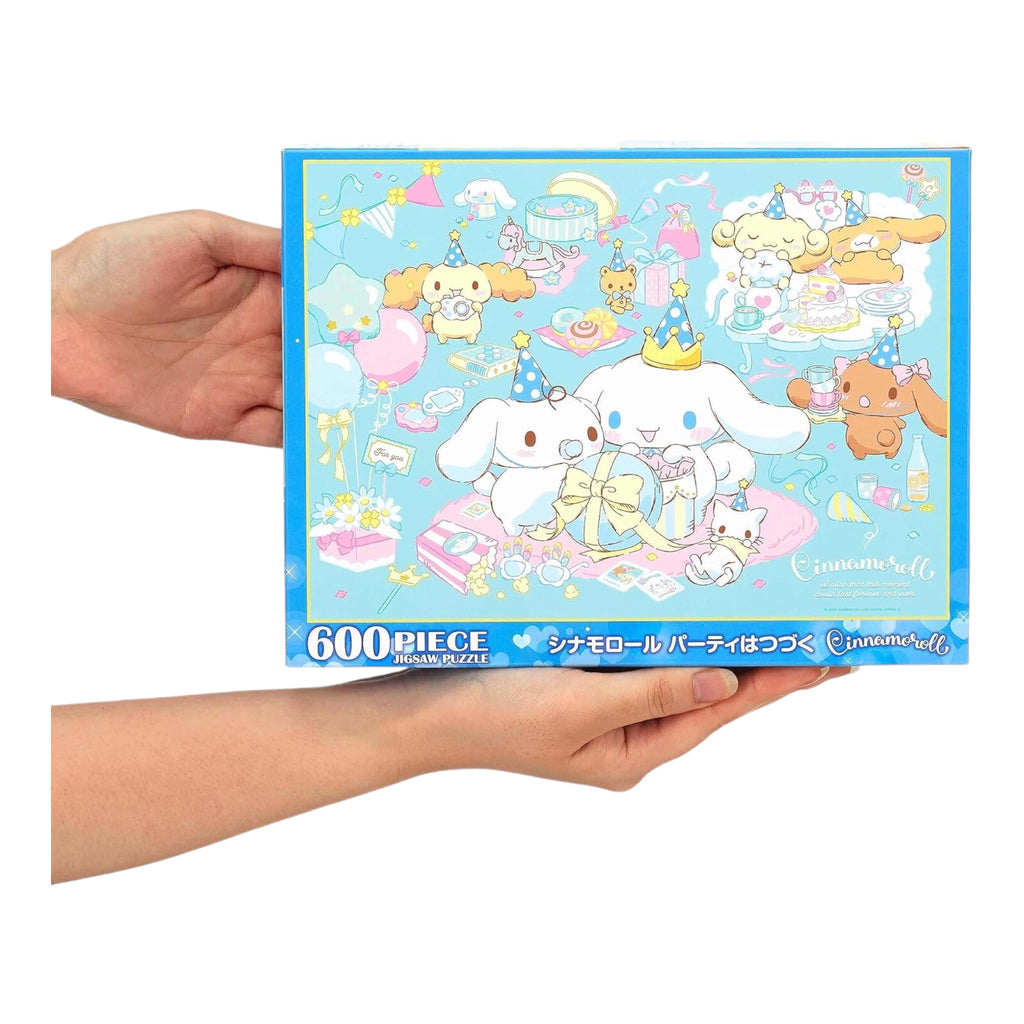 Sanrio Cinnamoroll Party Goes Ongoing 600-piece jigsaw puzzle box featuring Cinnamoroll and friends celebrating with gifts and party hats on a blue background.