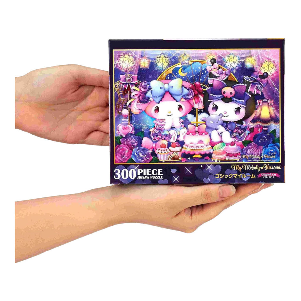 Hands holding a box of Sanrio My Melody & Kuromi 300-piece jigsaw puzzle with intricate fantasy artwork, illustrating the compact and gift-ready packaging